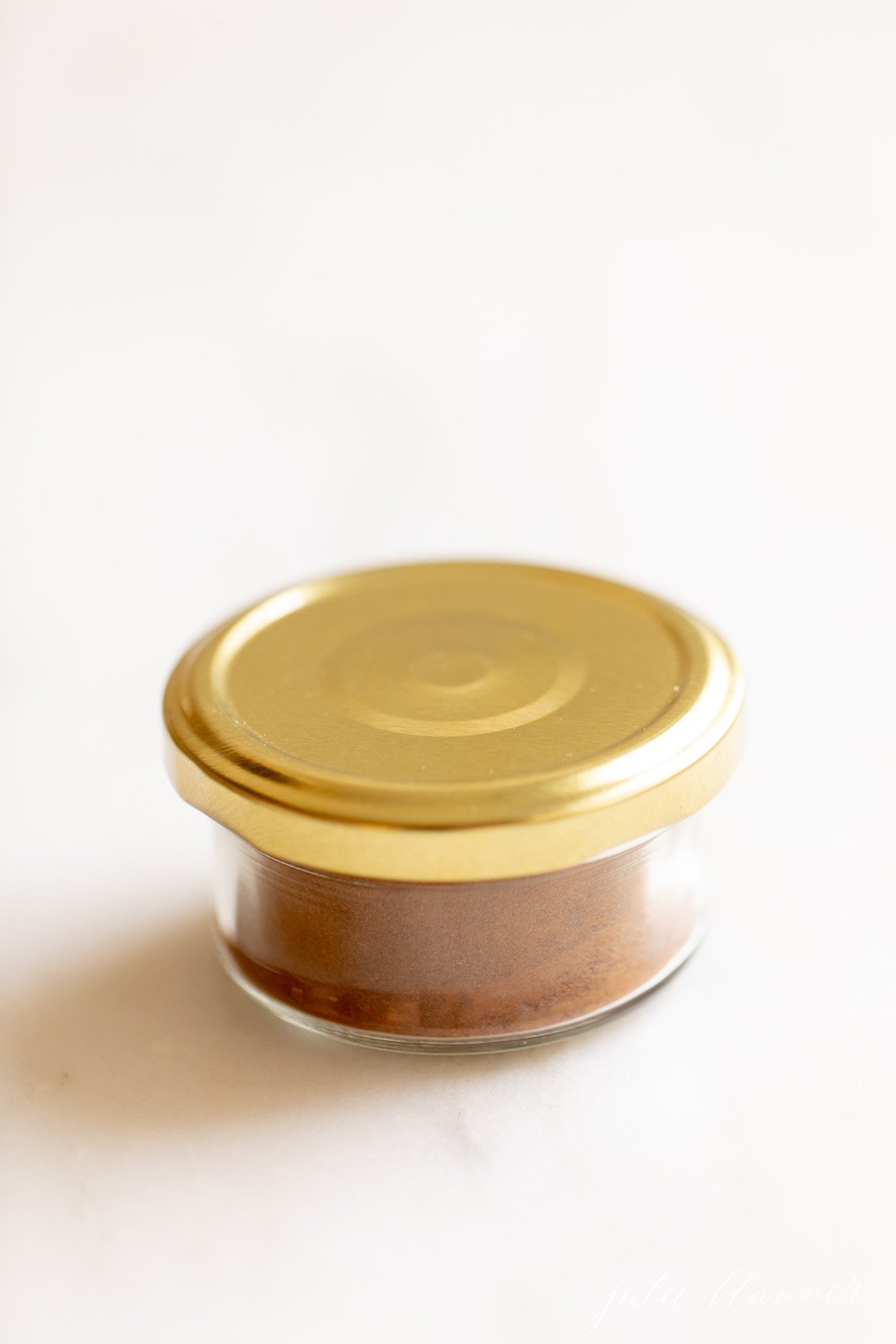 Homemade allspice blend in a small glass jar with a gold lid on a white countertop.