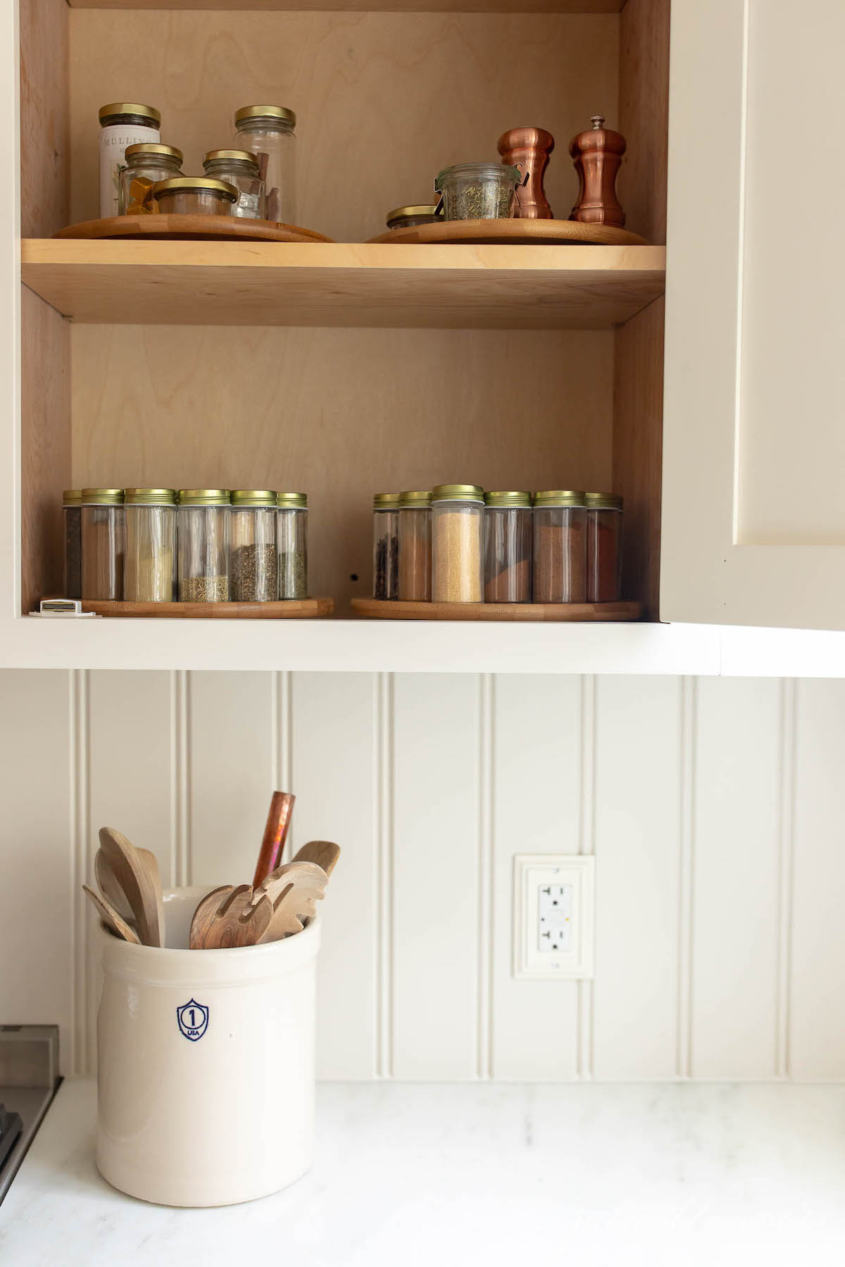 A white kitchen with a cabinet door open, looking into a collection of spices.