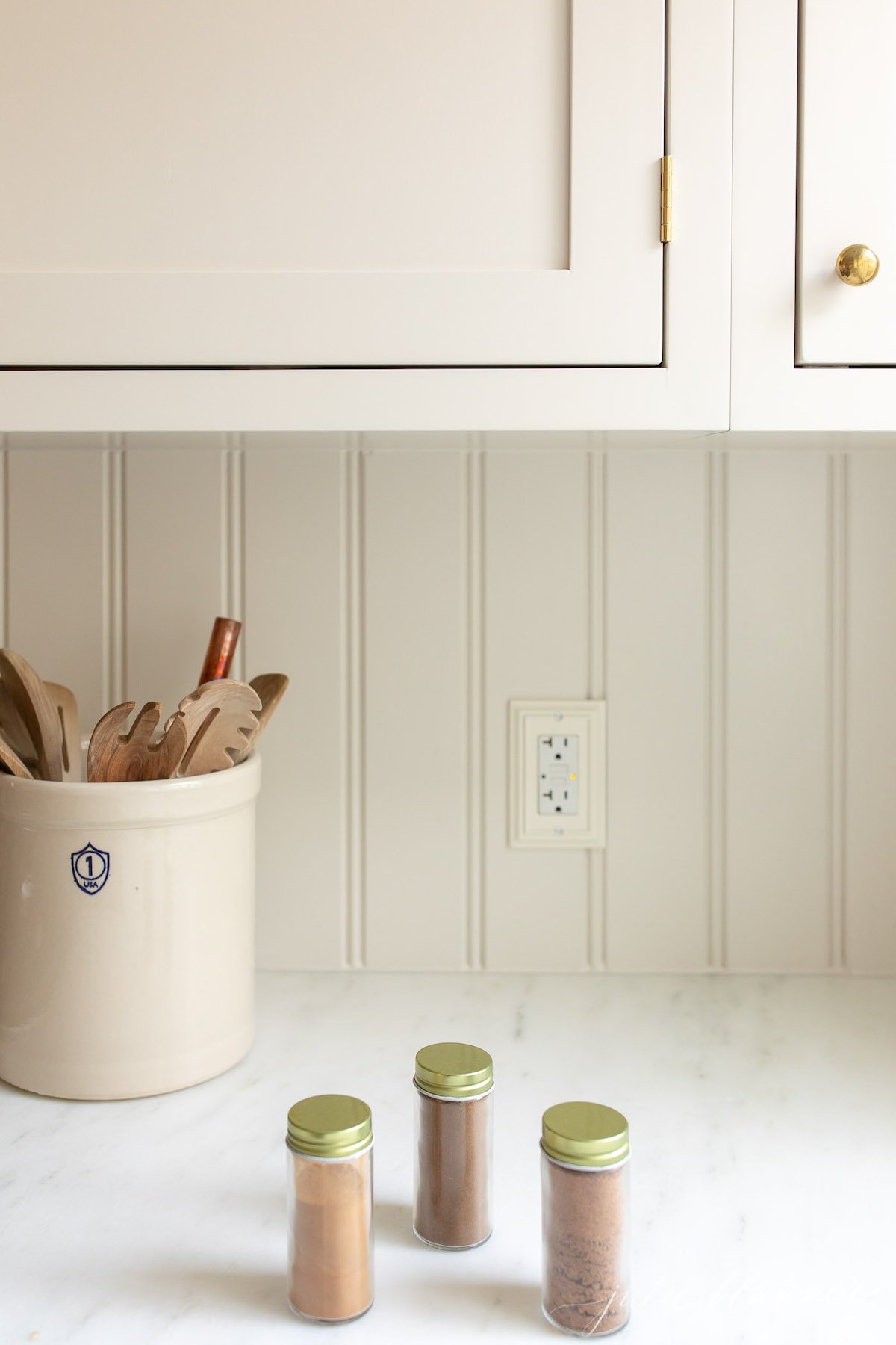 A white kitchen with 3 glass jars of spices for an allspice seasoning blend on the counter.