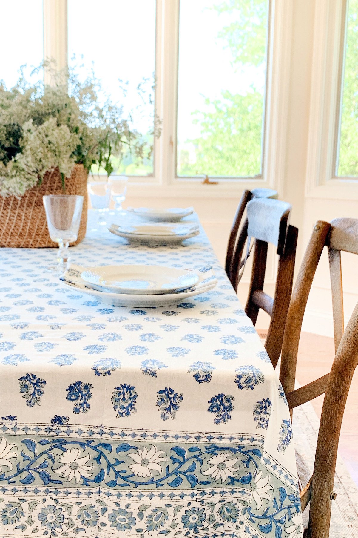 A blue and white block print tablecloth on a table surrounded by wood chairs.