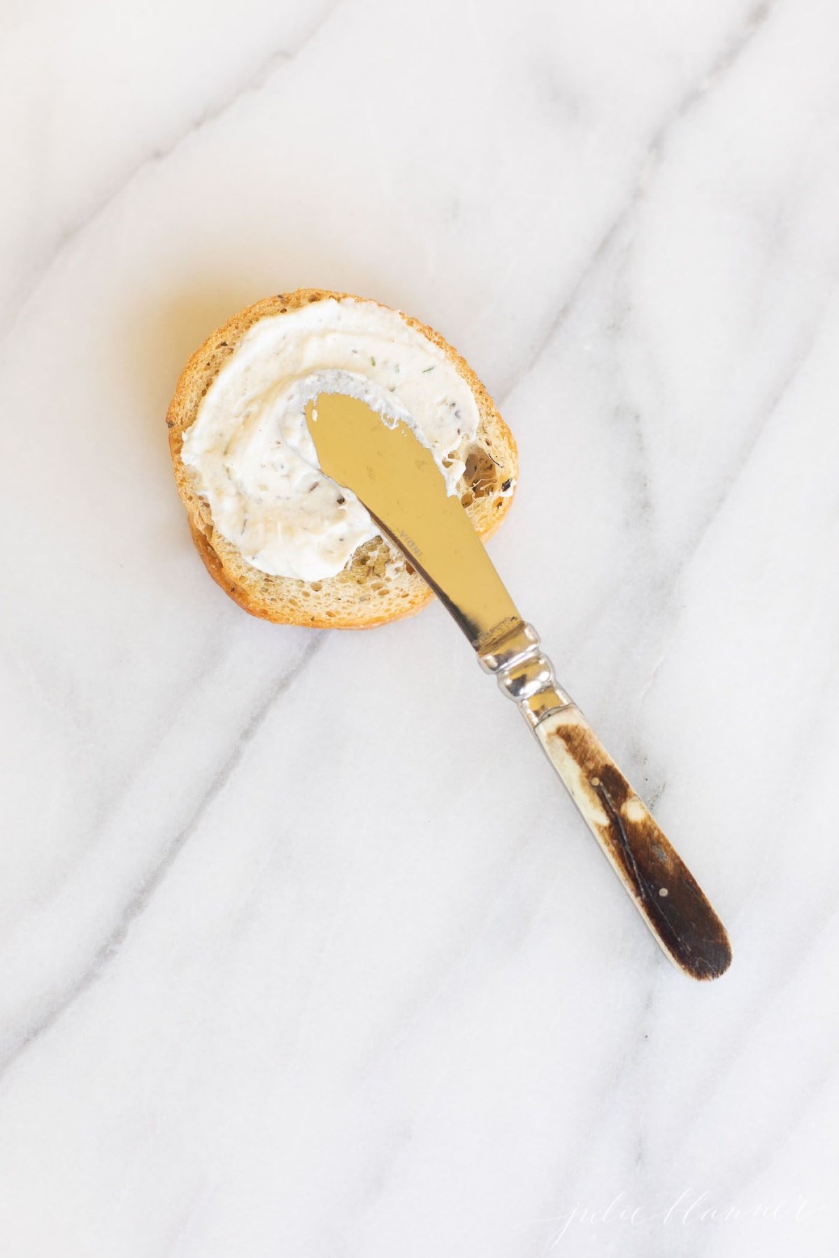 A spreader knife, spreading homemade Boursin cheese on a cracker.