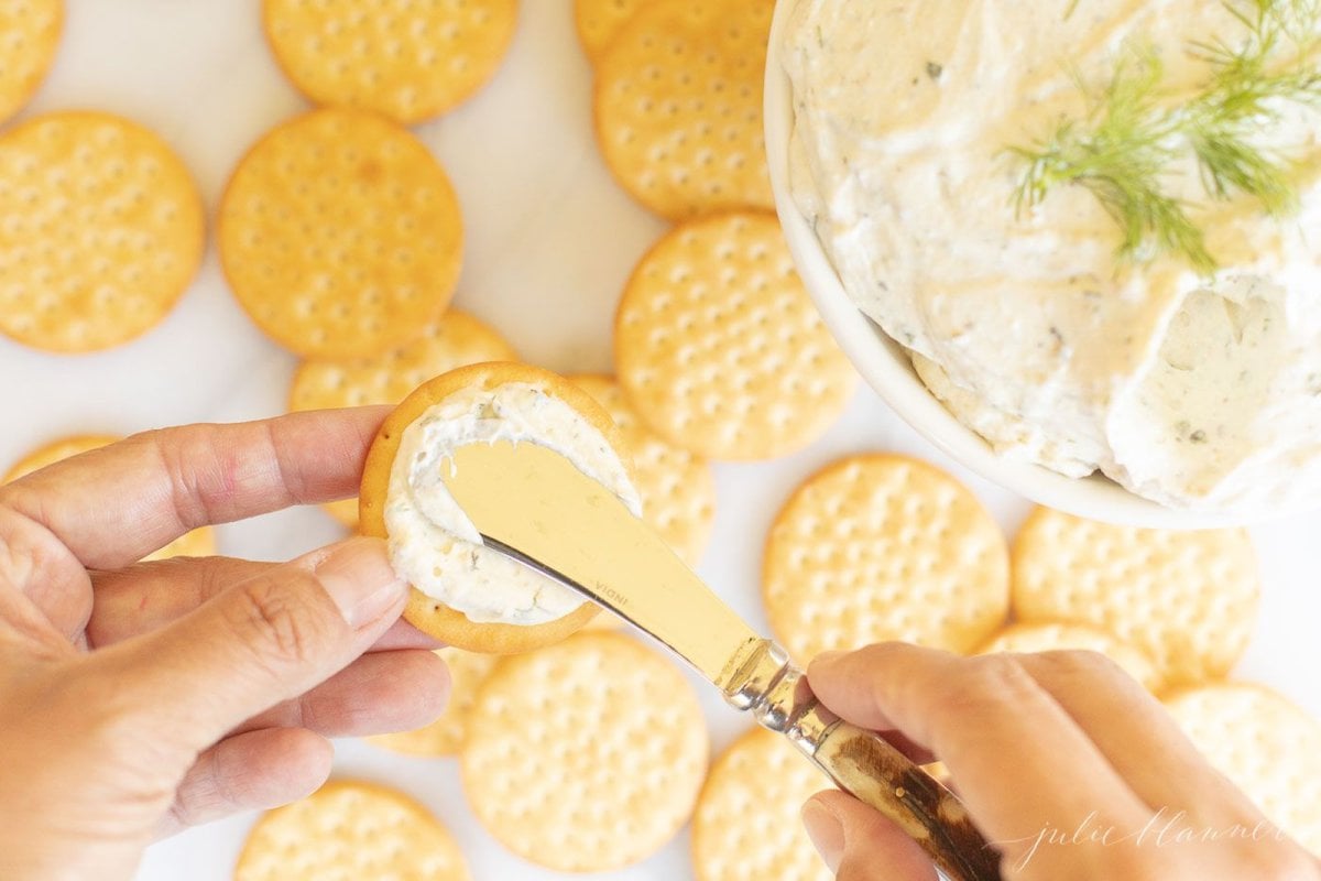 A spreader knife, spreading homemade Boursin cheese on a cracker.