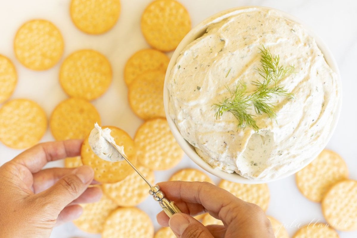 A spreader knife, spreading homemade Boursin cheese on a cracker.