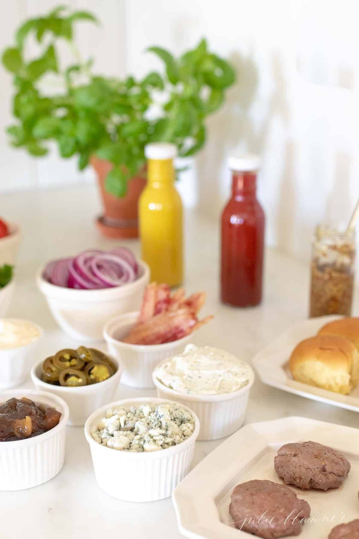 Burger toppings displayed in white ceramic bowls, condiments in rear and buns to the side. #burgerbar #burgershop #sliderbar