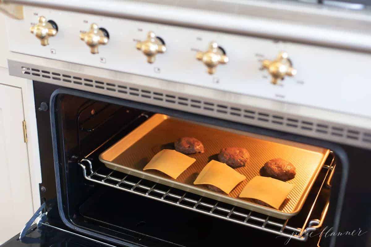 Burger patties on a baking sheet, going into the oven. Half have cheese, half do not. 