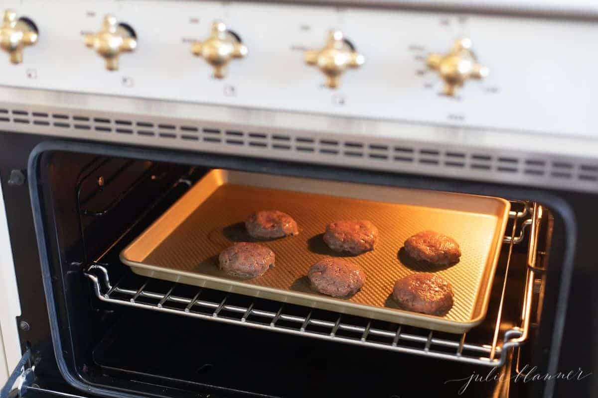 Burger patties on a baking sheet, going into the oven.