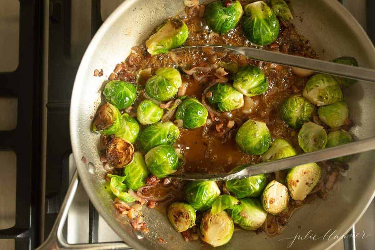 Crispy brussel sprouts ingredients in a pan, tongs in the center. 