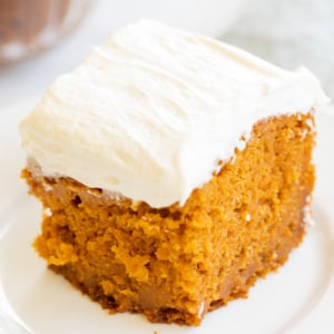 A slice of pumpkin cake with fluffy cream cheese frosting on a white plate.