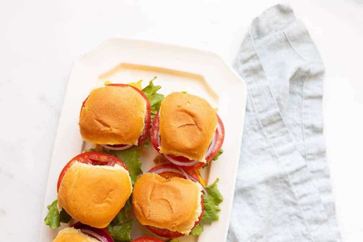 White platter of prepared burgers, blue linen napkin to the side.