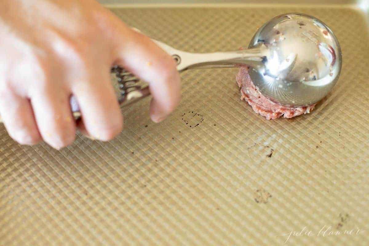 Burgers being scooped onto baking sheets using an ice cream scooper. 