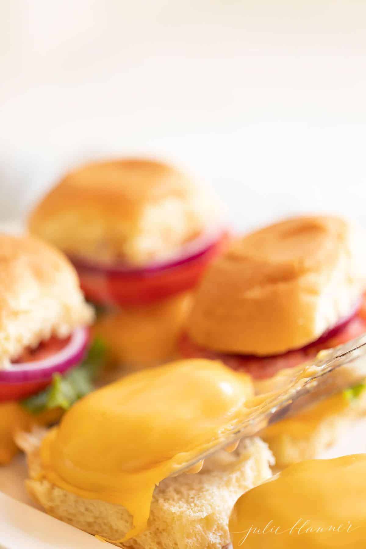 Burgers stacked with lettuce, tomato and onion on a white platter. #burgersintheoven