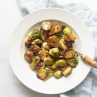 White bowl with sauteed brussel sprouts, blue linen napkin to the side.