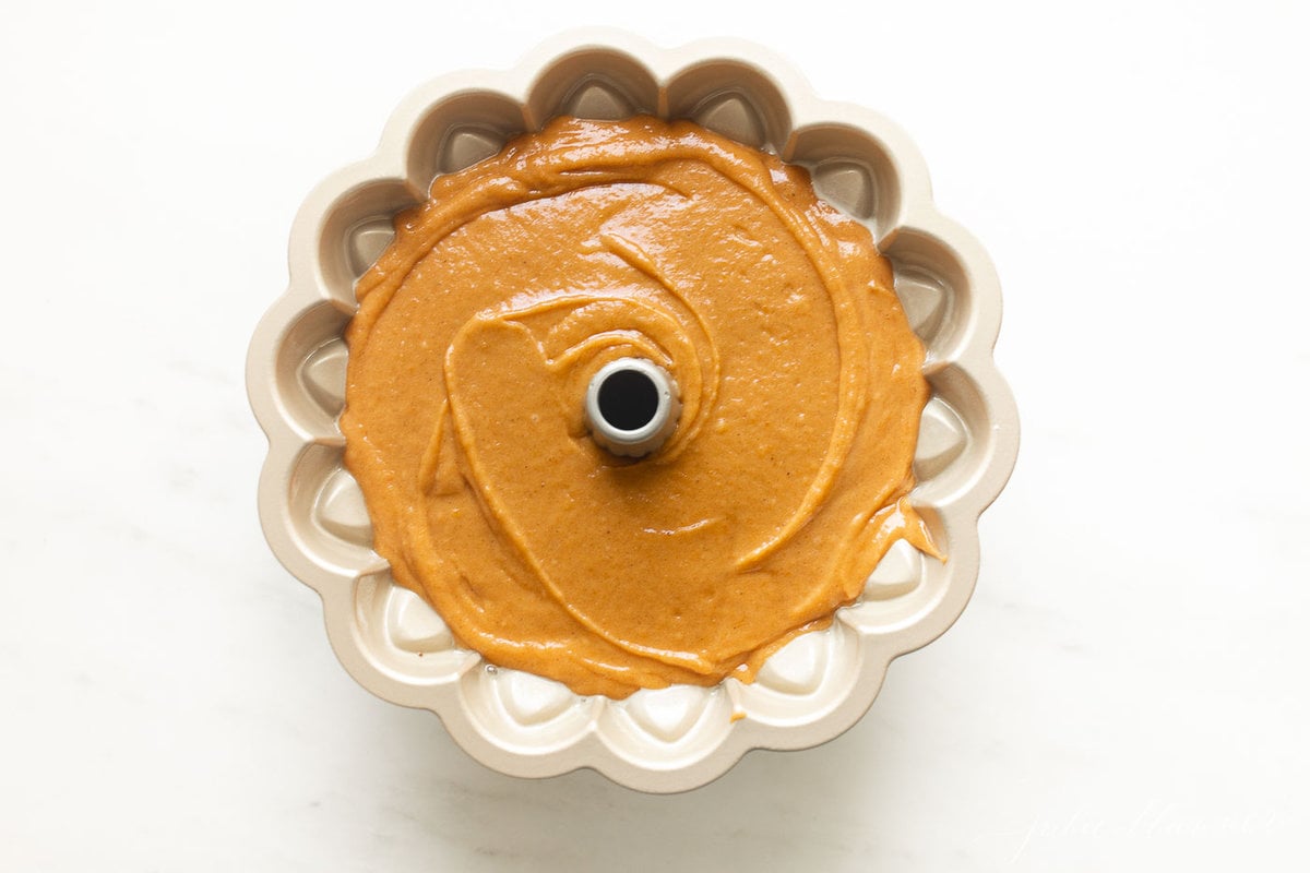 A pumpkin bundt cake recipe inside a bundt cake pan, on a white surface.