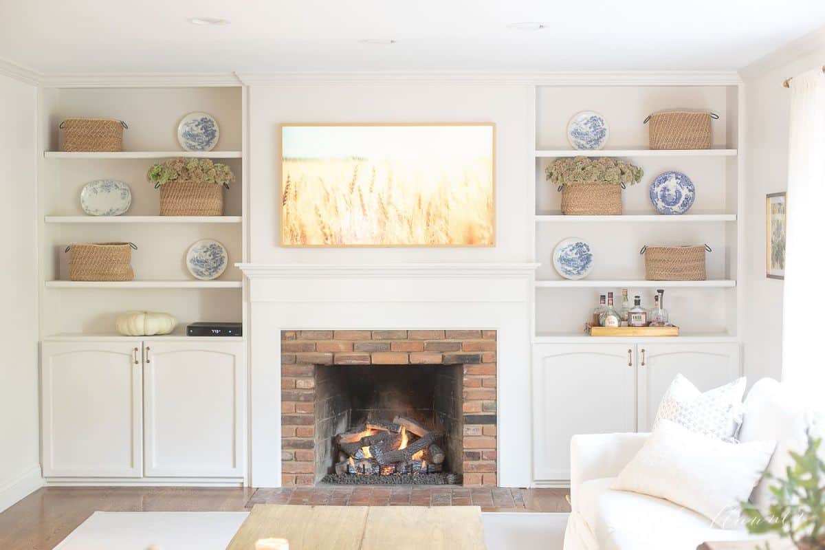 Living room fireplace burning with artwork above and bookshelves on each side. #falllivingroom