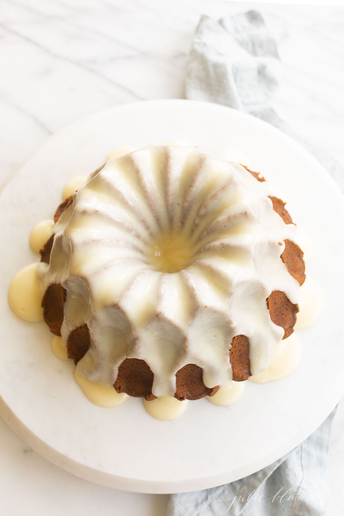 A frosted pumpkin bundt cake on a white marble surface.