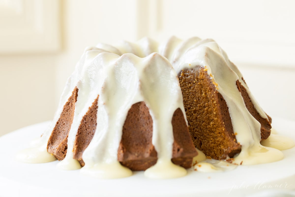 A frosted pumpkin bundt cake on a white marble surface.