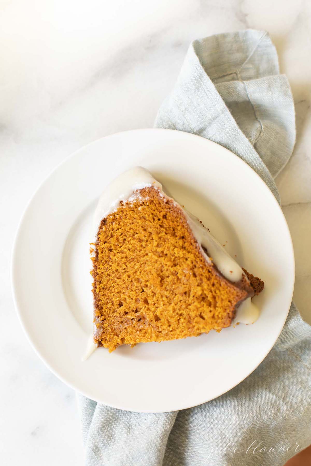 A slice of pumpkin bundt cake on a white plate with a blue linen napkin under it.