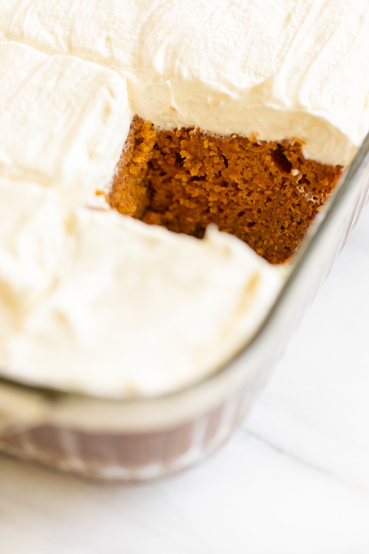 A slice of pumpkin cake removed from a glass pan full of cake.