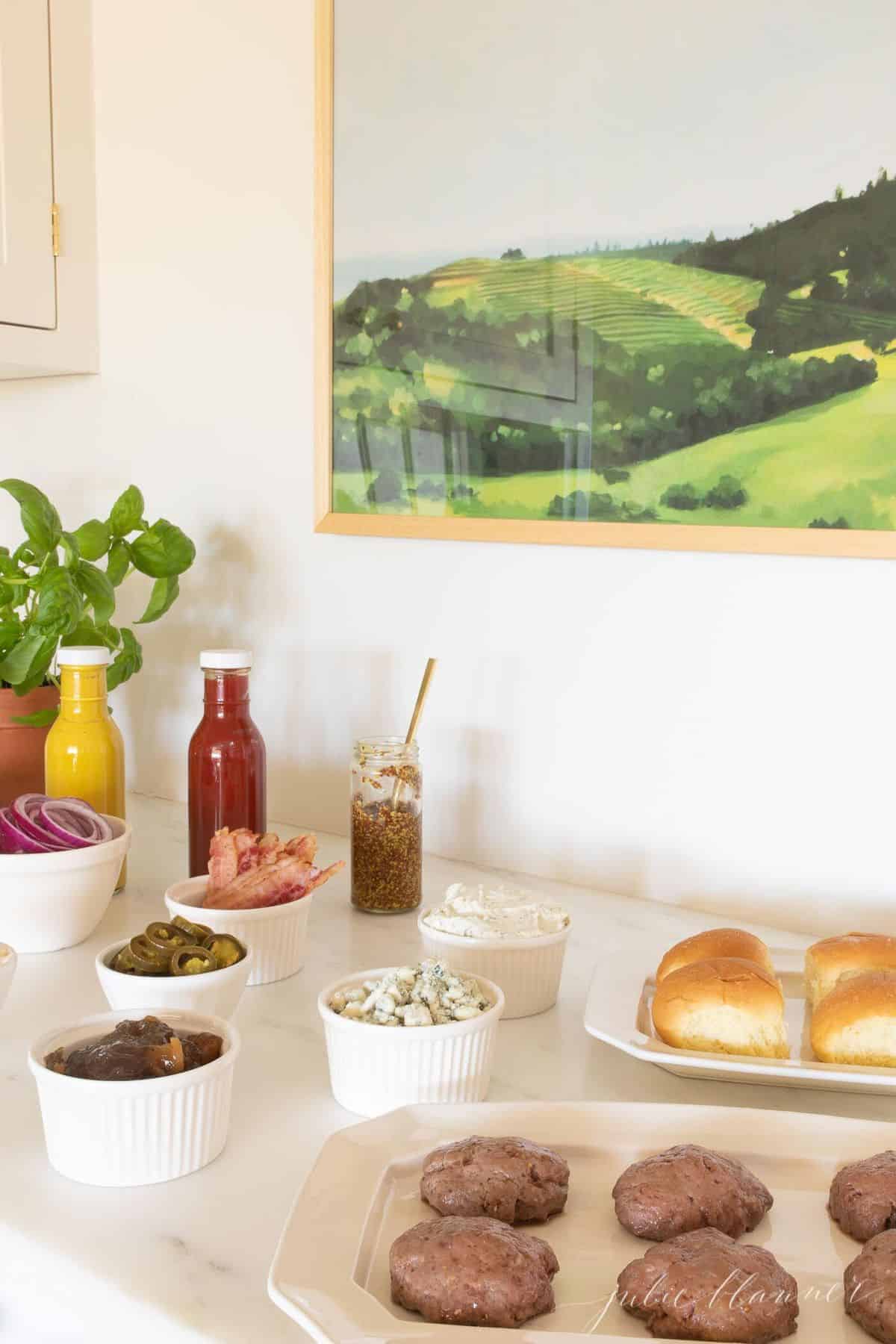 Burger toppings displayed in white ceramic bowls, condiments in rear and buns to the side. #burgerbar #burgershop #sliderbar