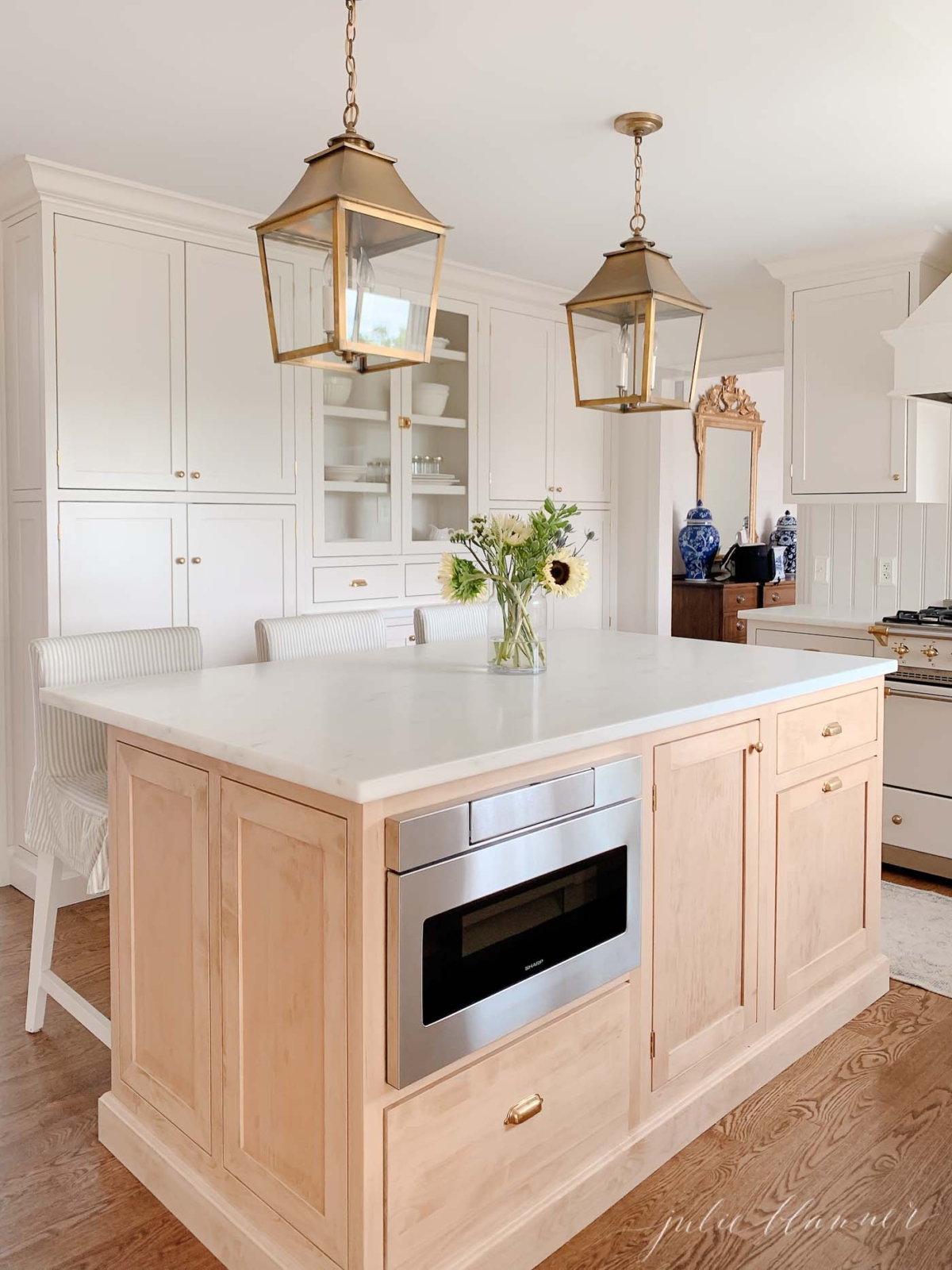 A classic kitchen with cream cabinets, brass hardware and brass lanterns and an under counter microwave drawer.