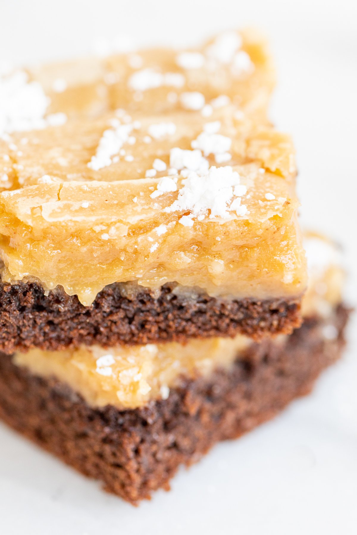 Two slices of ooey gooey butter cake stacked on a white surface.