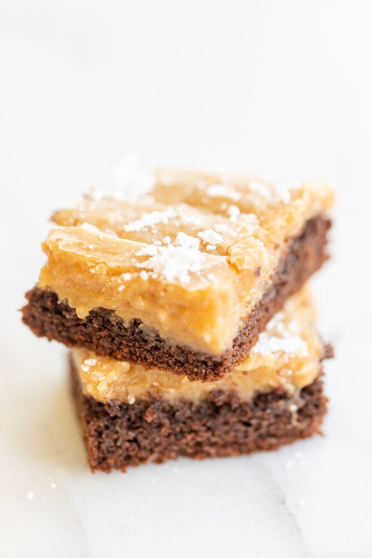 Two slices of ooey gooey butter cake stacked on a white surface.