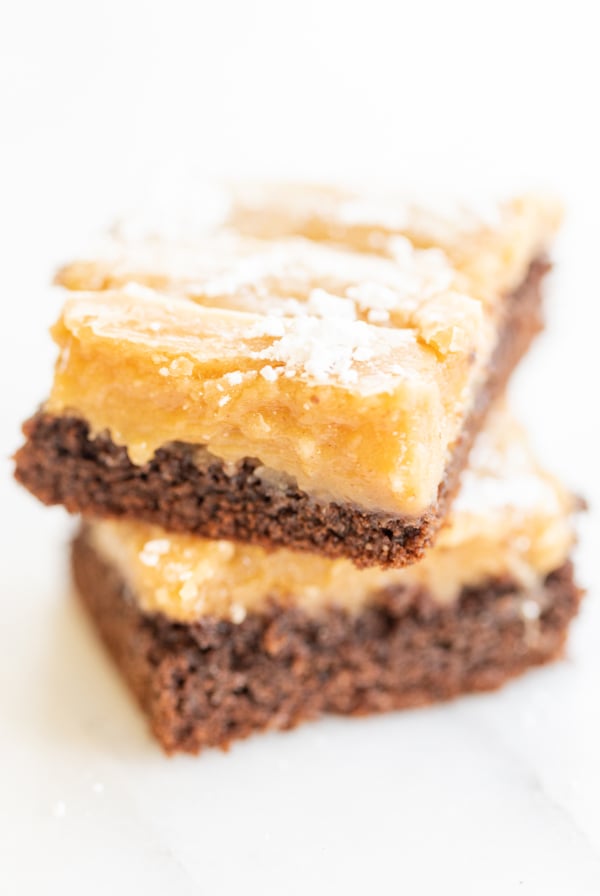 Two slices of ooey gooey butter cake stacked on a white surface.