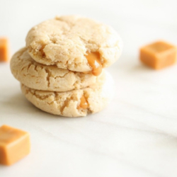 A stack of caramel stuffed cheesecake cookies on a marble countertop.