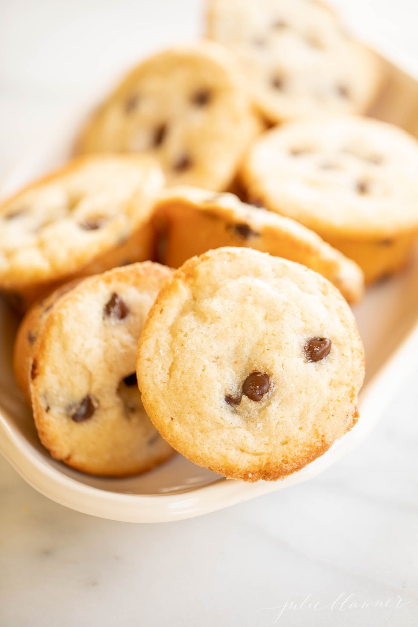 A white platter full of mini chocolate chip muffins.