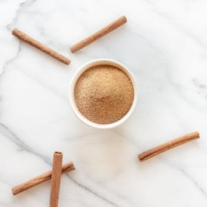 A jar of cinnamon sugar, cinnamon sticks scattered around.