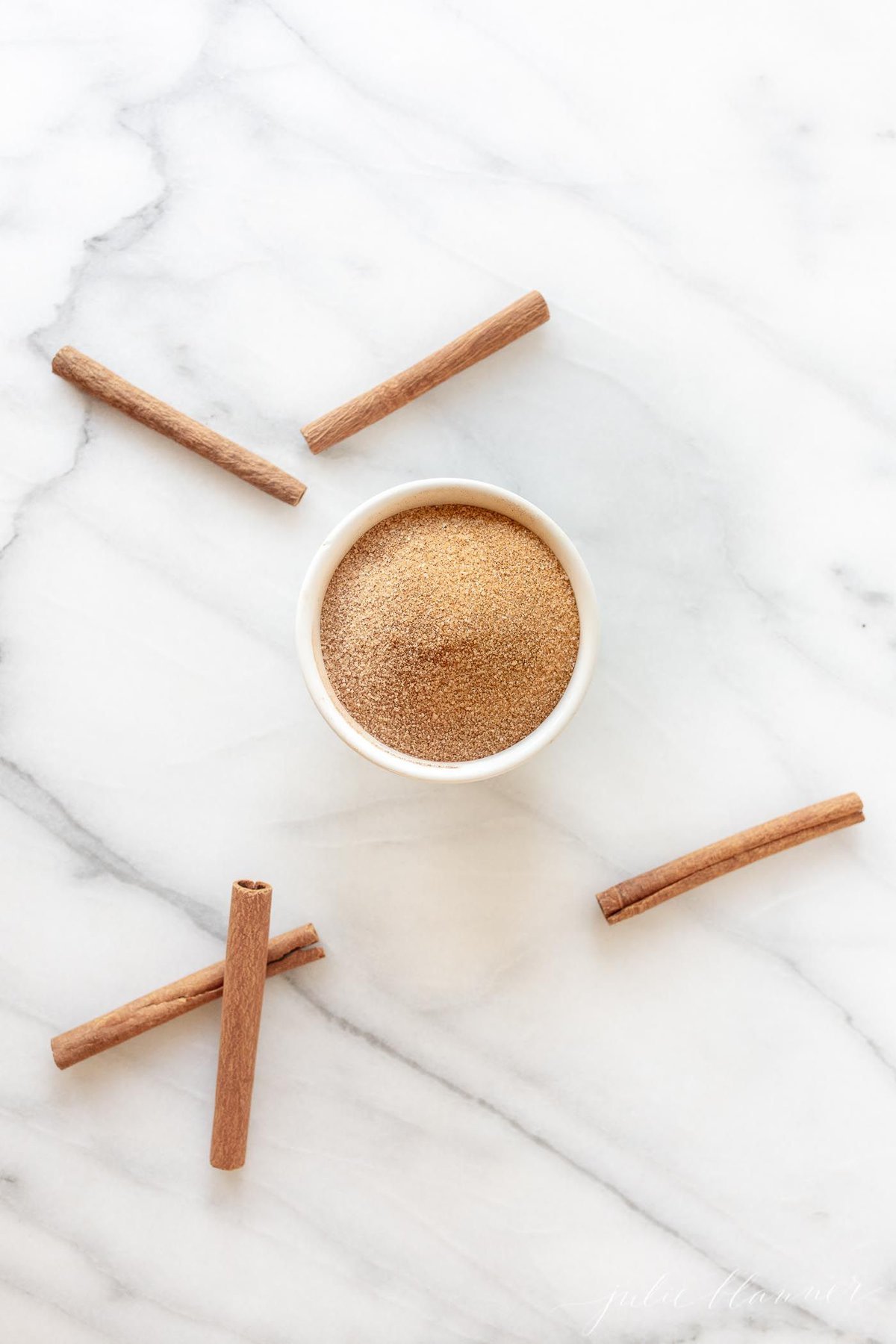 A jar of cinnamon sugar, cinnamon sticks scattered around.