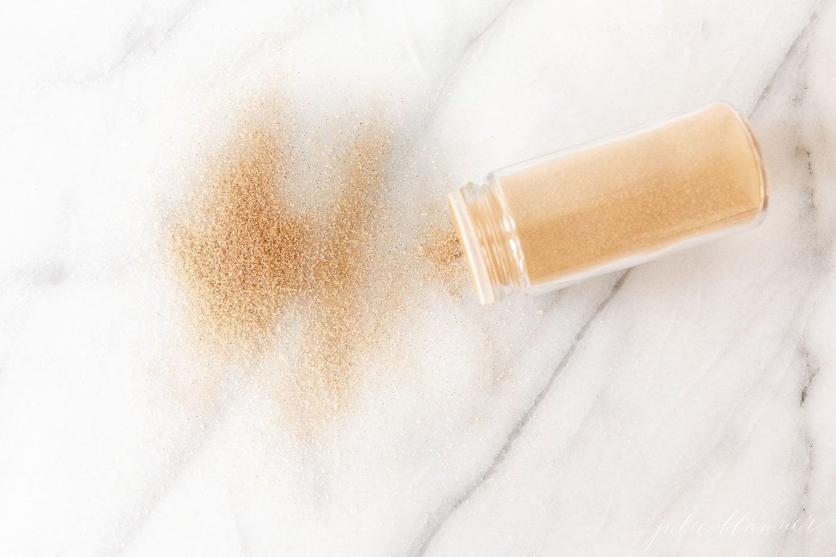 An open bottle of homemade cinnamon sugar, some scattered onto the marble countertop.