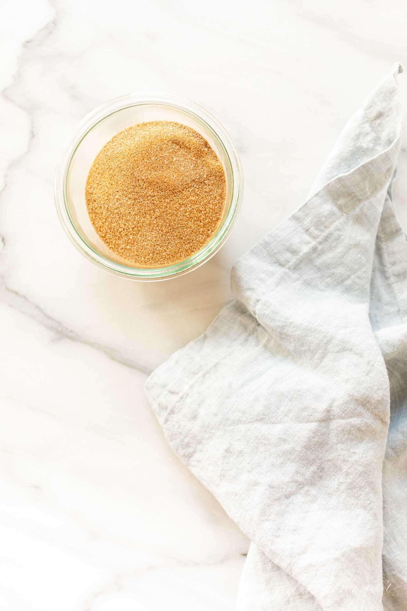 A small glass jar full of a homemade cinnamon sugar recipe, on a marble countertop.