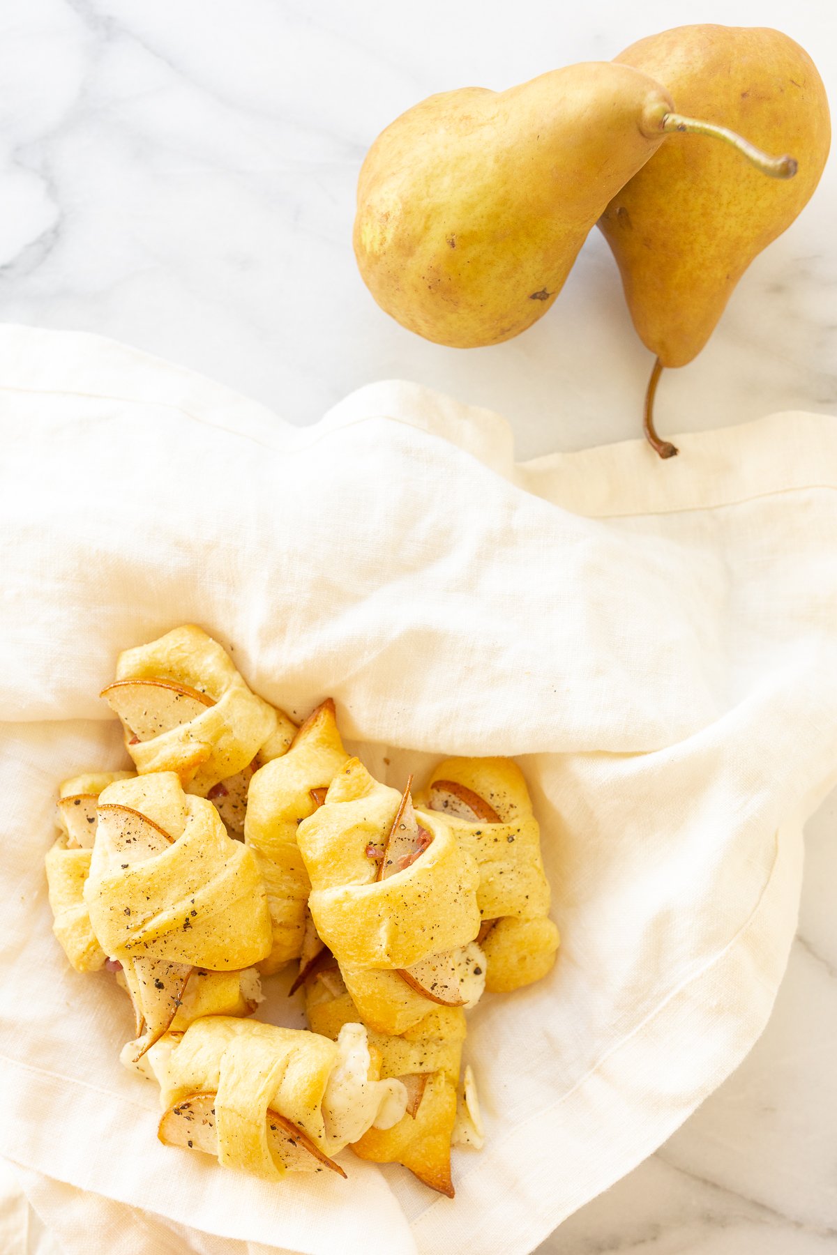 A white napkin featuring crescent roll appetizers with pears on it.