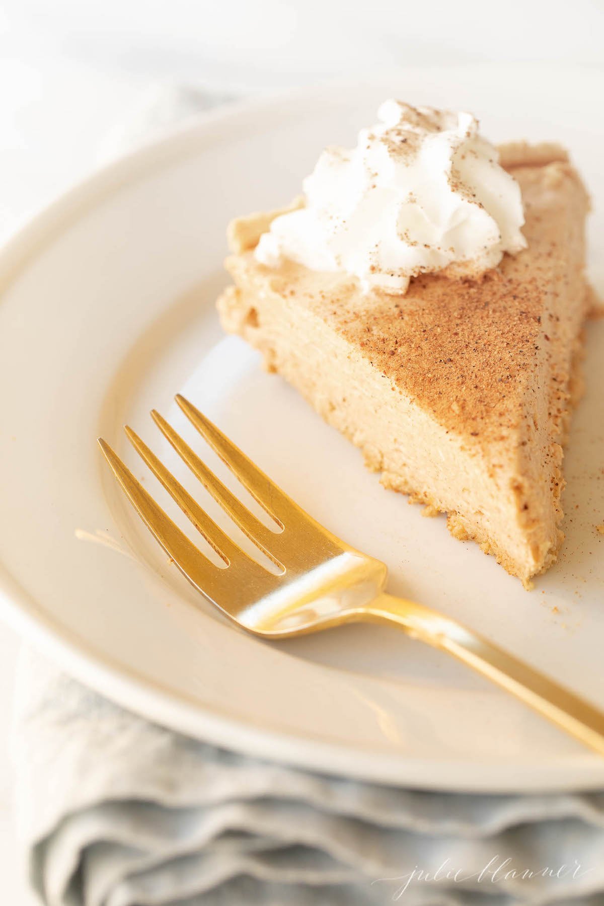 Pumpkin cheesecake topped with whipped cream on a white plate with a gold fork to the side.