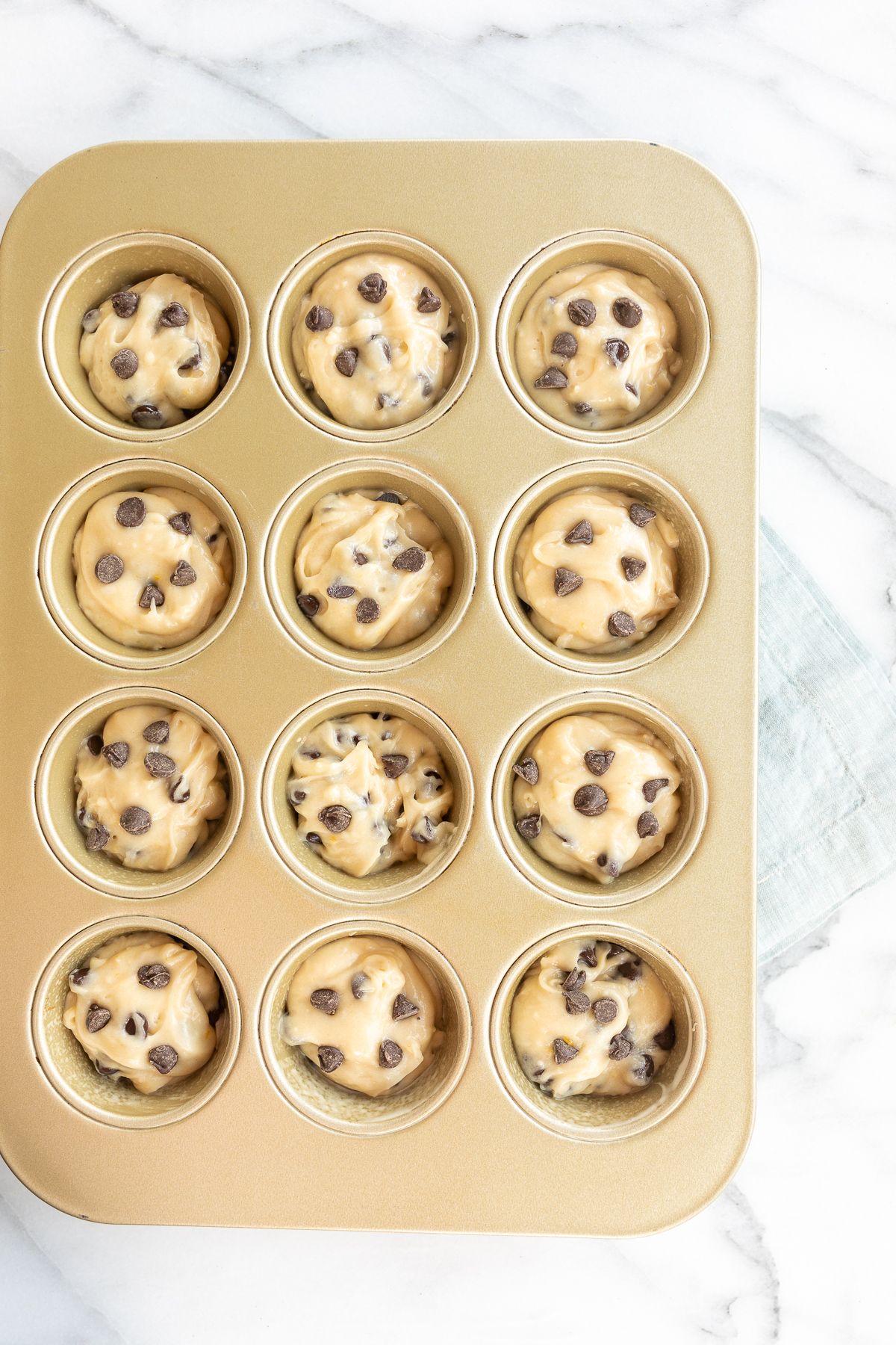 A gold mini muffin tin full of batter for a chocolate chip muffin recipe.