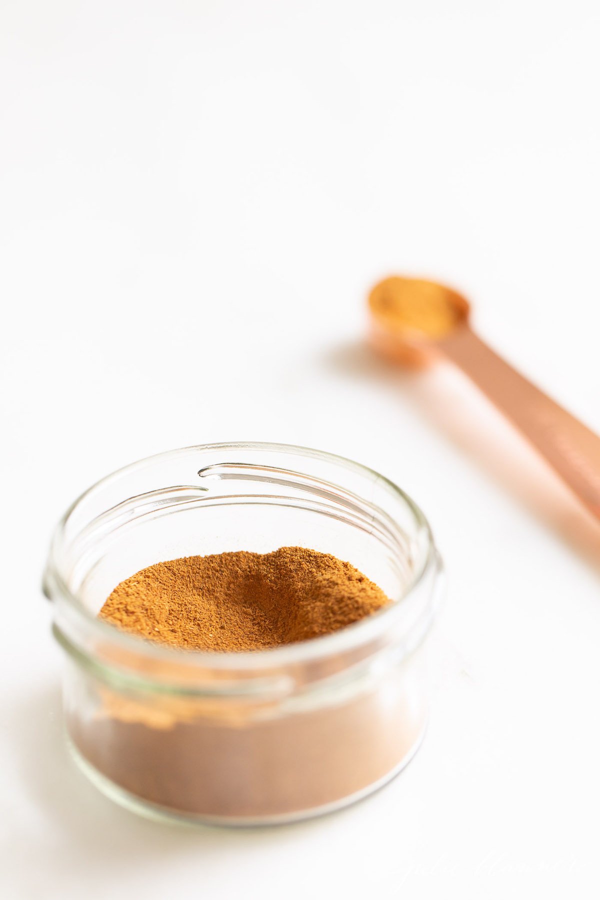 A small clear jar of pumpkin pie spice on a white countertop.