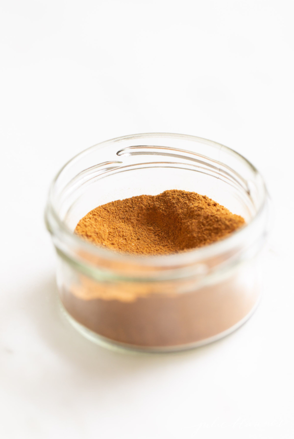 A small clear jar of pumpkin pie spice on a white countertop.