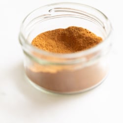 A small clear jar of pumpkin pie spice on a white countertop.