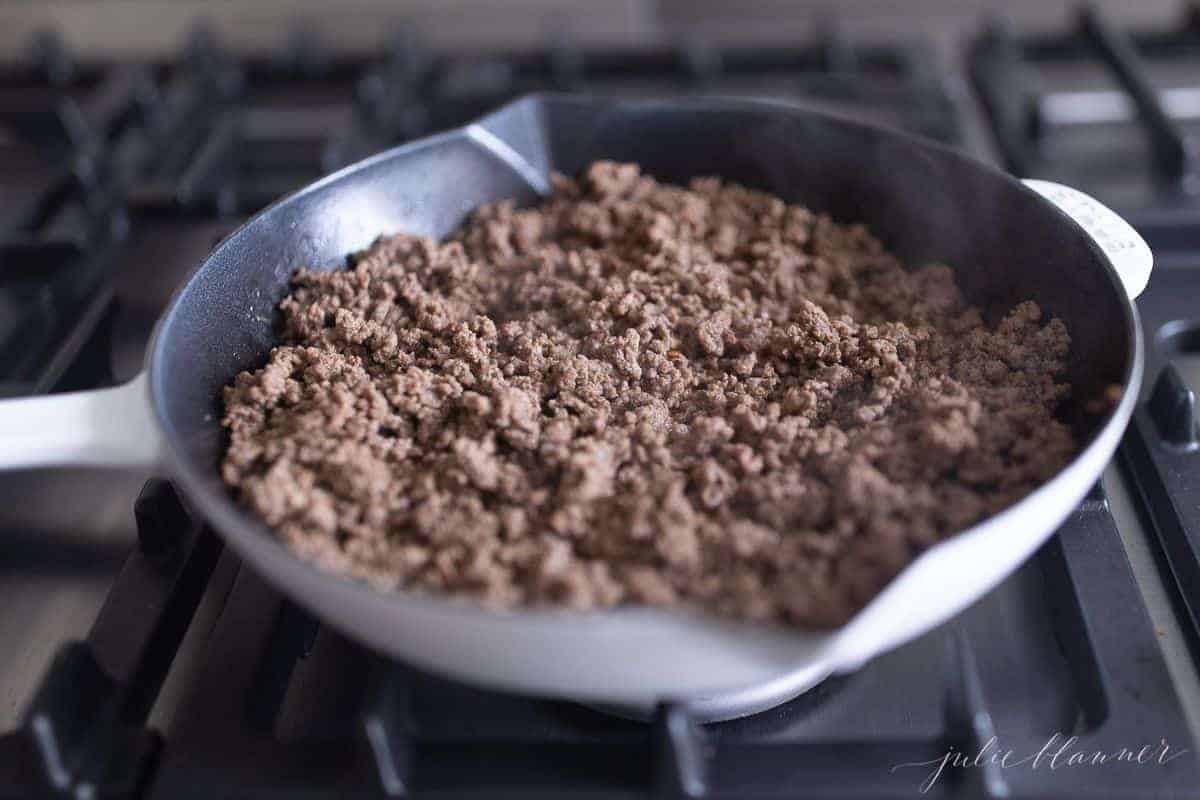 Stovetop, with a skillet with fully cooked ground beef.