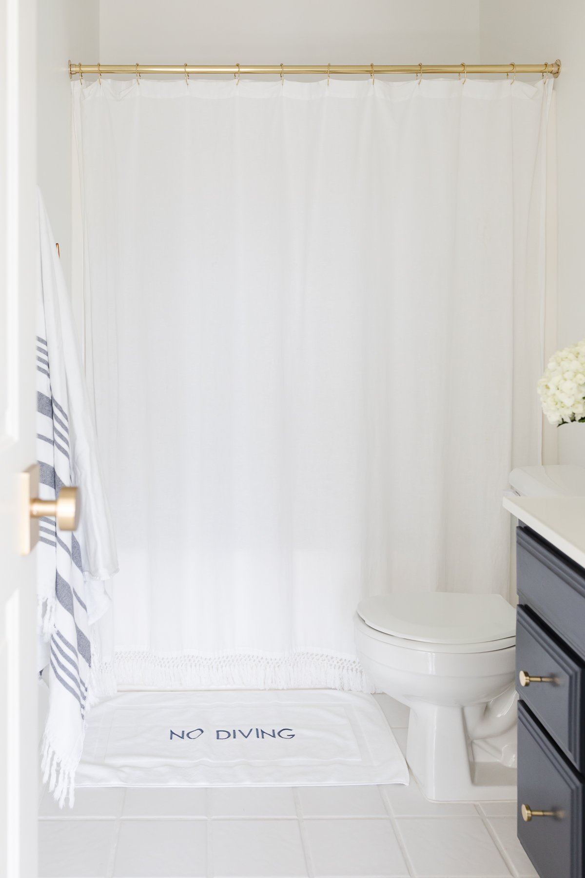 A nautical bathroom with a navy vanity and a rattan round mirror.