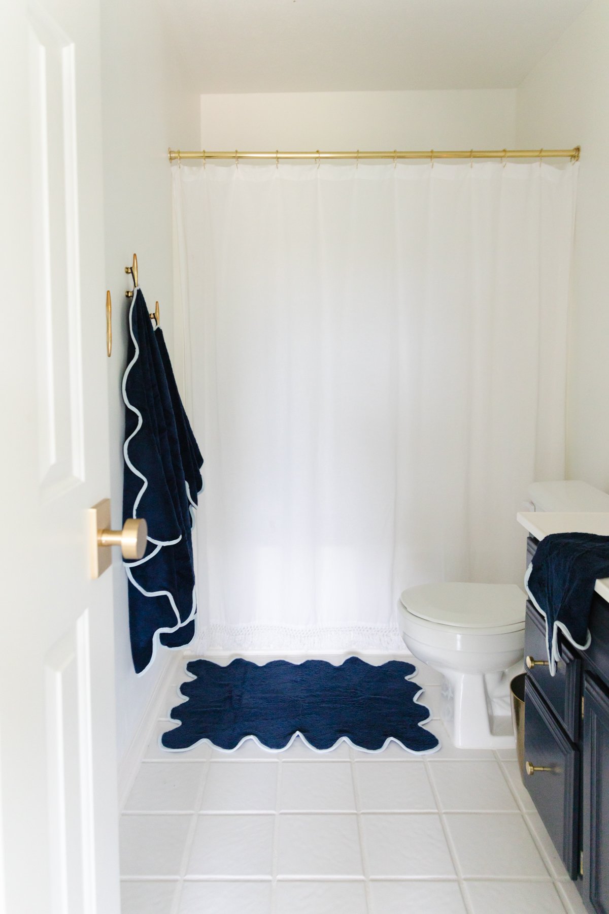 A nautical-themed bathroom with a white shower curtain and a blue rug.