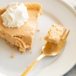Pumpkin cheesecake topped with whipped cream on a white plate with a gold fork to the side.
