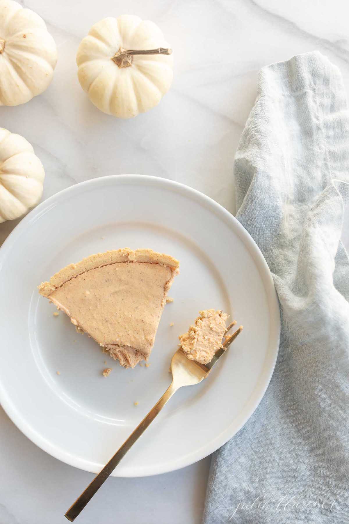 Pumpkin cheesecake topped with whipped cream on a white plate with a gold fork to the side.