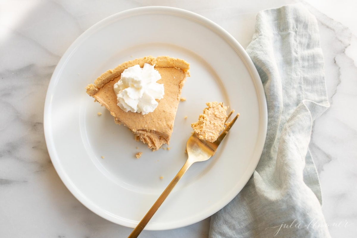 Pumpkin cheesecake topped with whipped cream on a white plate with a gold fork to the side.