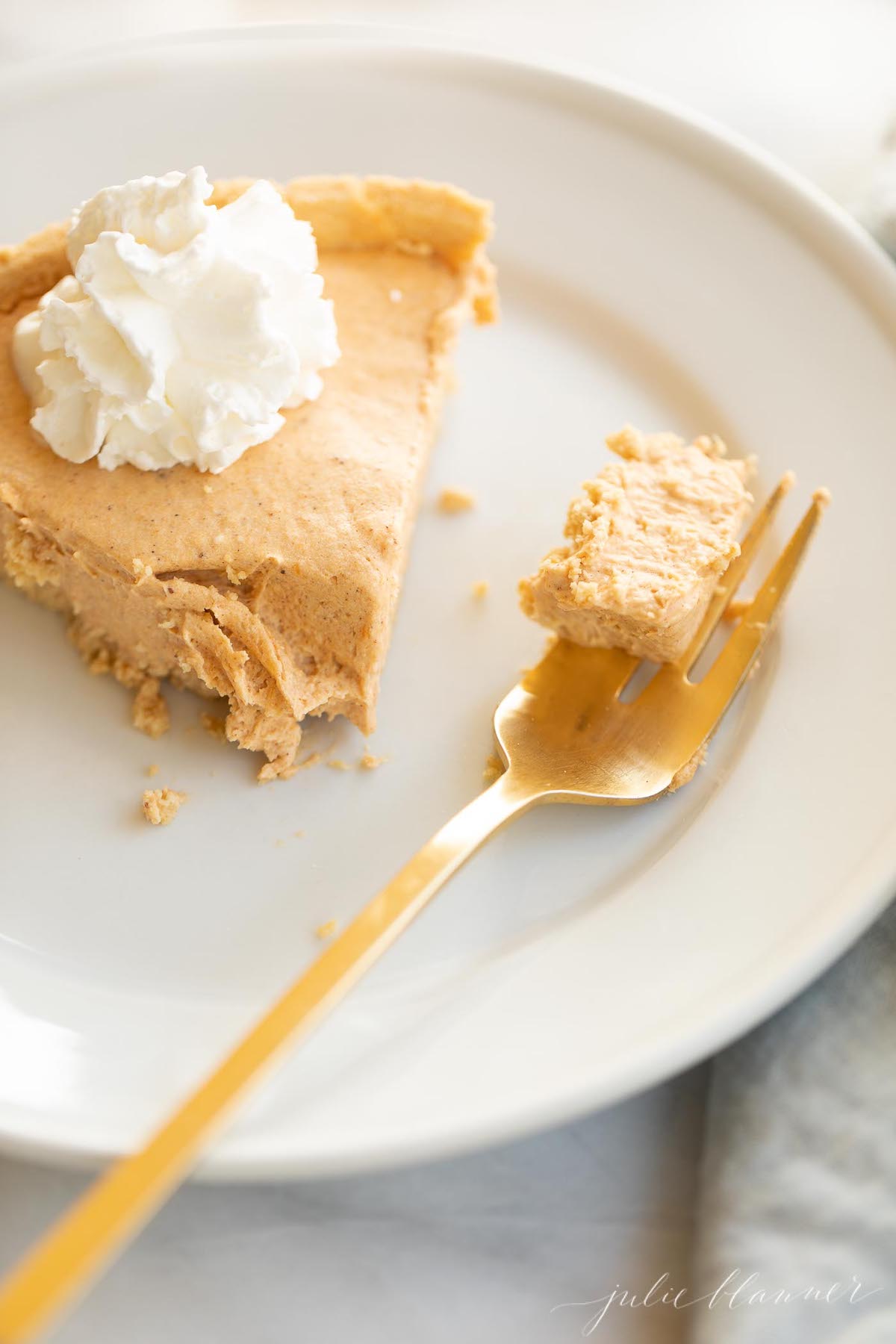 Pumpkin cheesecake topped with whipped cream on a white plate with a gold fork to the side.