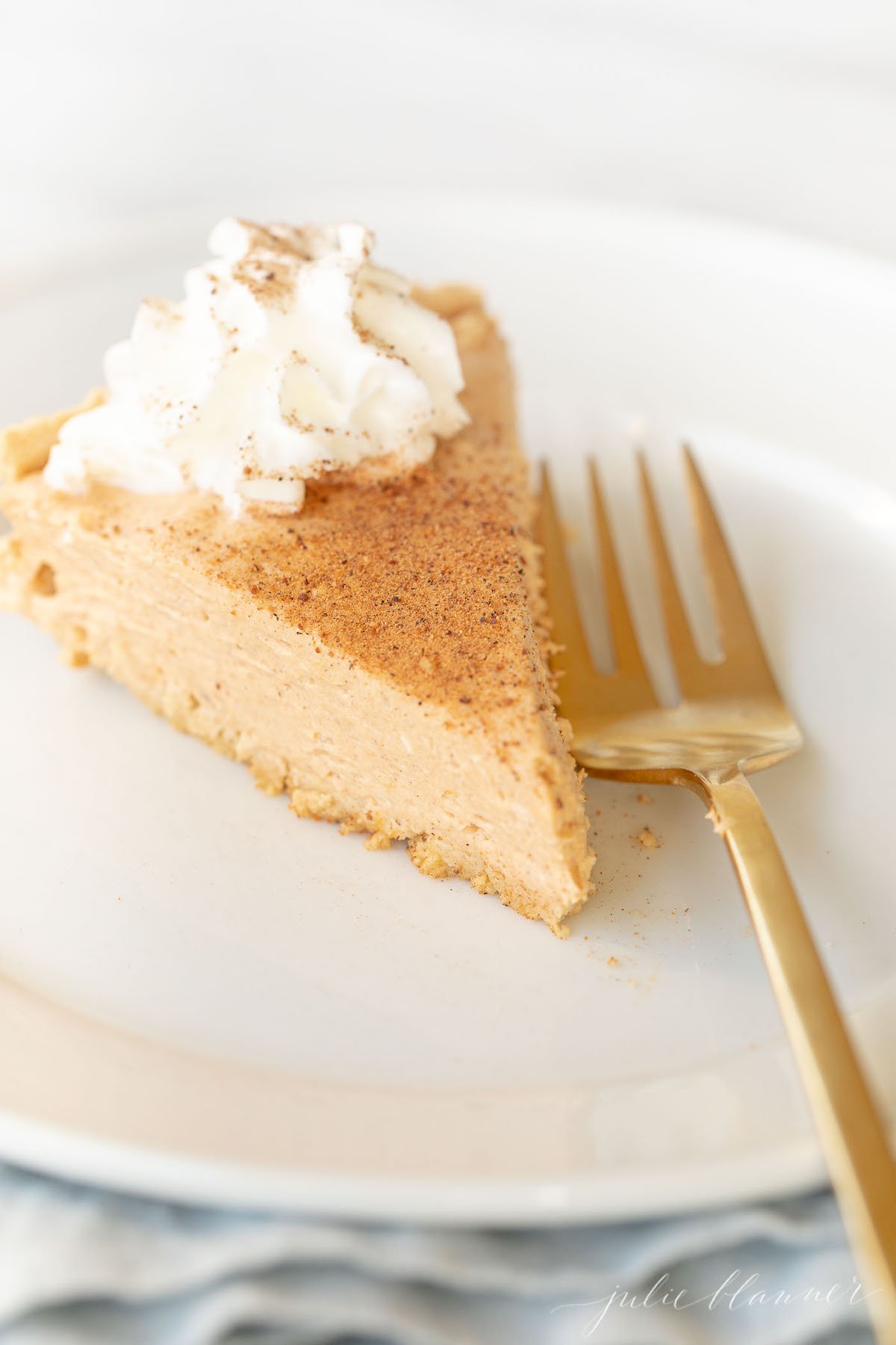 Pumpkin cheesecake topped with whipped cream on a white plate with a gold fork to the side.