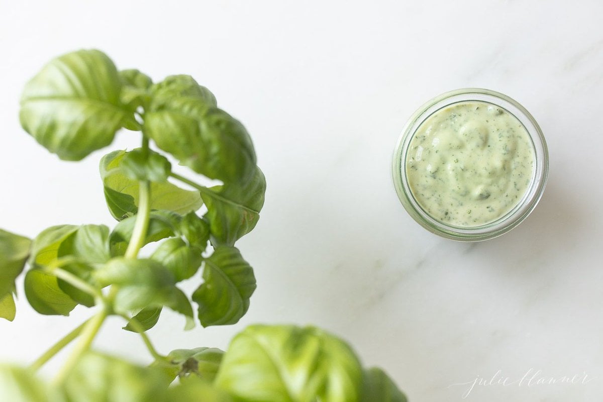 Fresh basil leaves next to a glass jar of basil aioli.