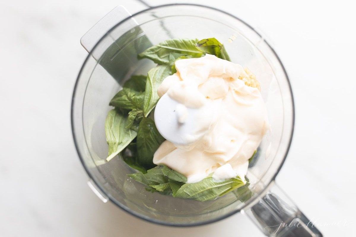 Basil and mayo inside a food processor for a pesto style basil aioli recipe.