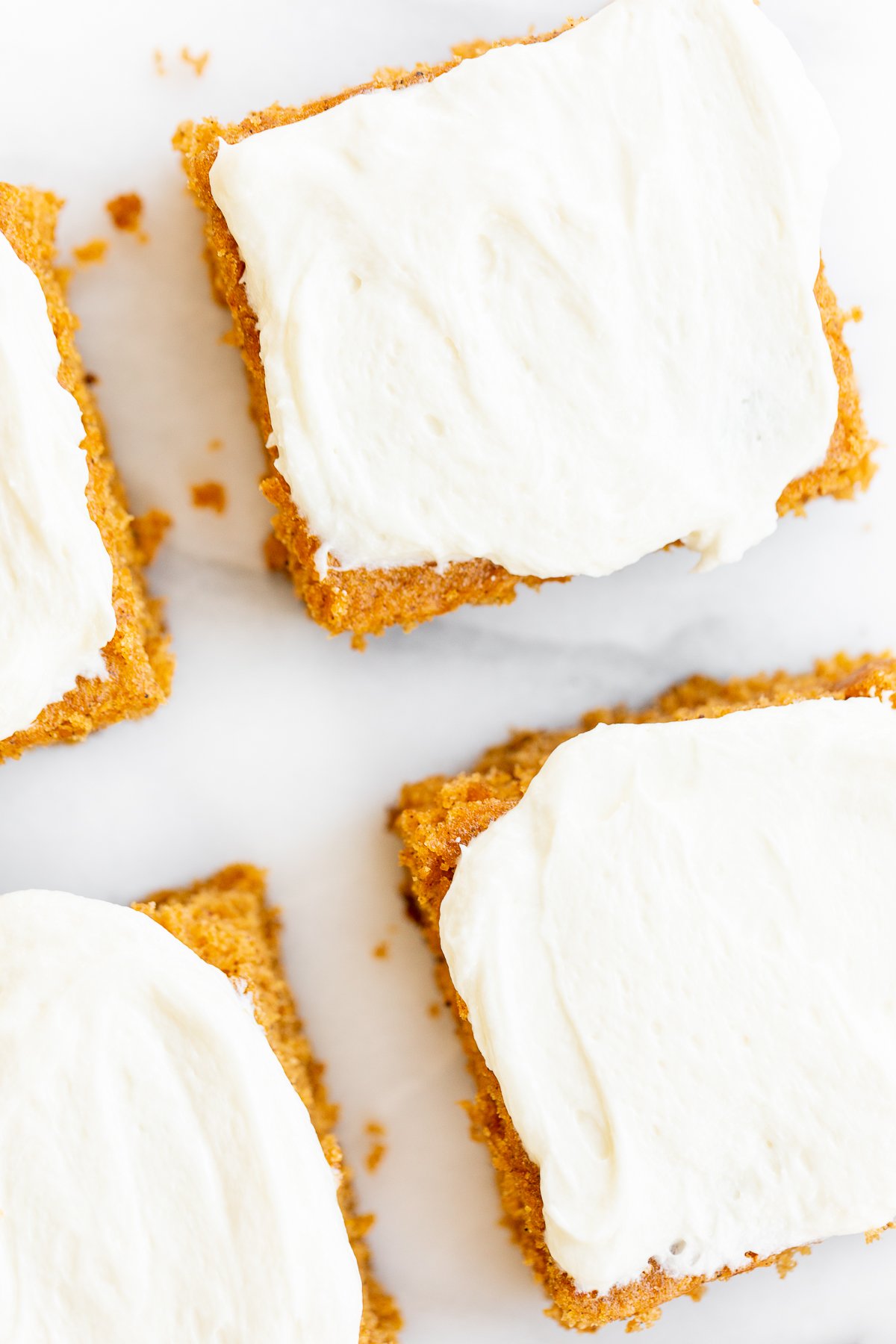 Pumpkin bars with cream cheese frosting on a marble surface.